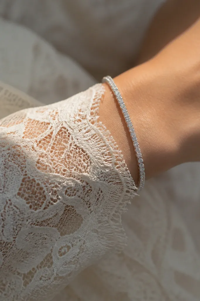 Close-up of a wrist with a slim crystal tennis-style bracelet over a long lace sleeve cuff, showing tiny stones catching light.