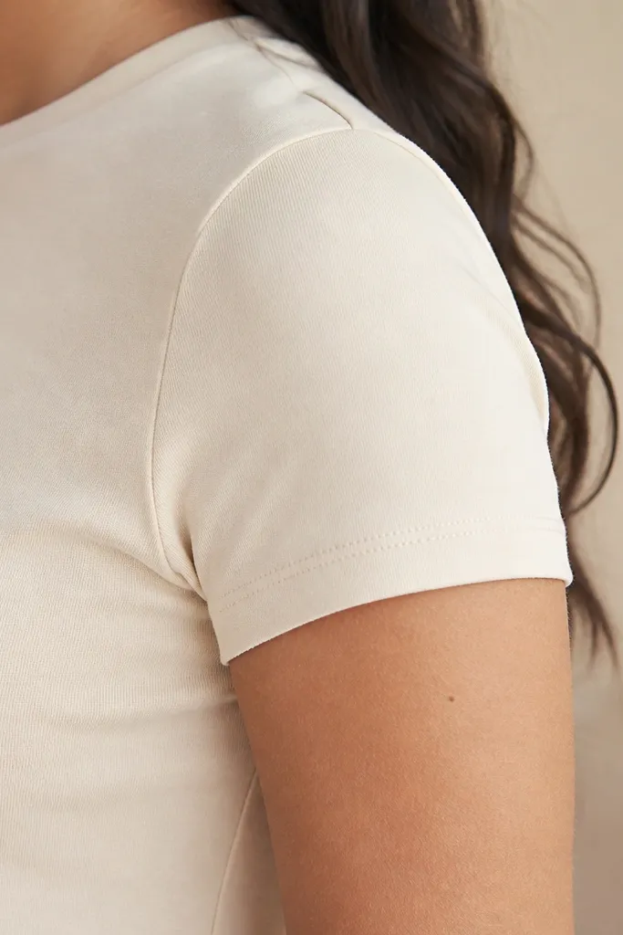 A close-up of a model’s upper arm and shoulder showing the sleeve seam sitting neatly at the natural shoulder line, with fabric lying flat and no visible stretching across the bicep.