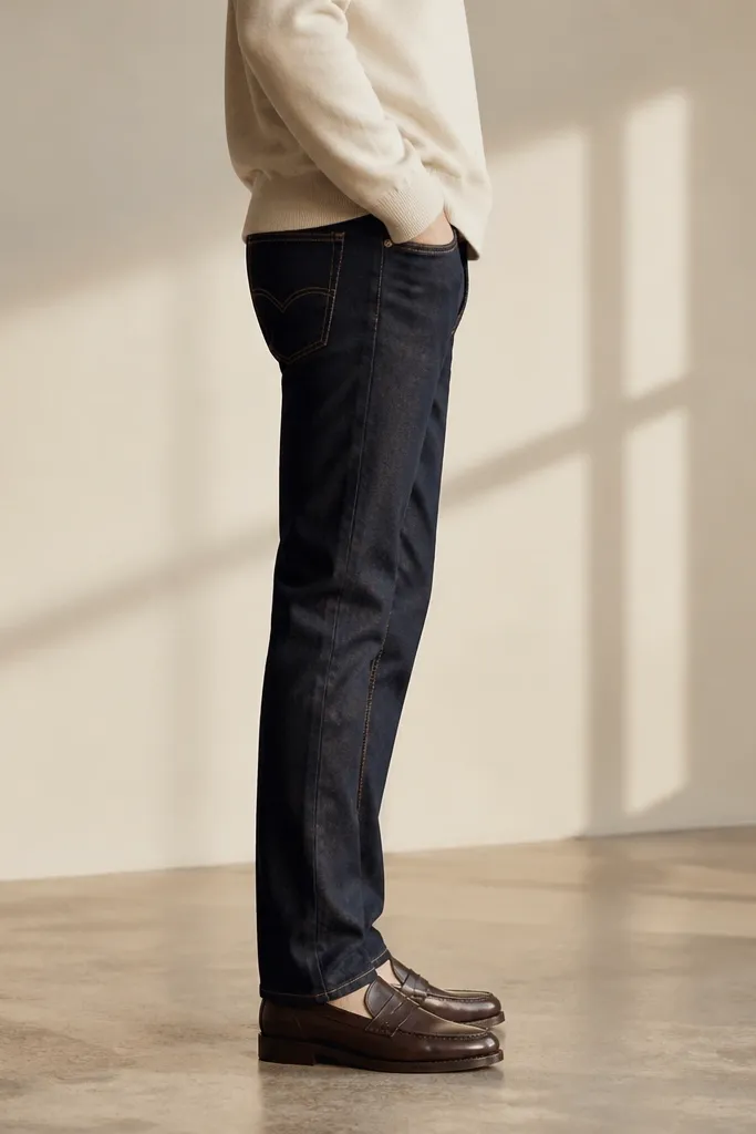 A side profile of dark jeans on a model with a tailored thigh and a hem break that sits neatly above the shoe.