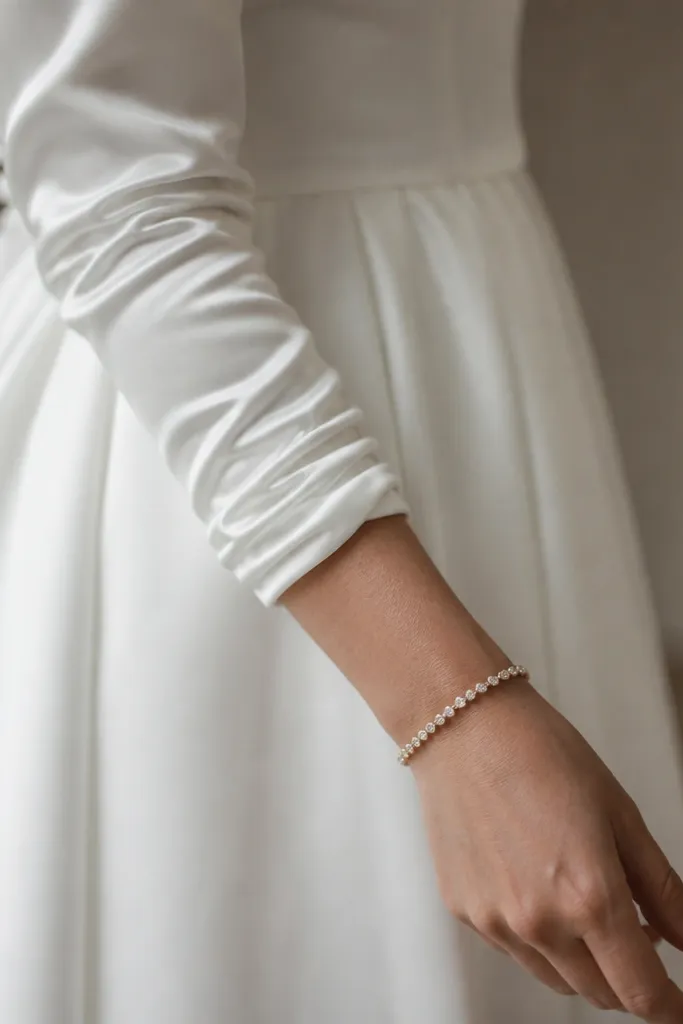 A long sleeve wedding dress close-up showing a sleeve ending above the wrist with visible wrinkling and bunching at the cuff, paired with a delicate bracelet that sits over the wrinkles.