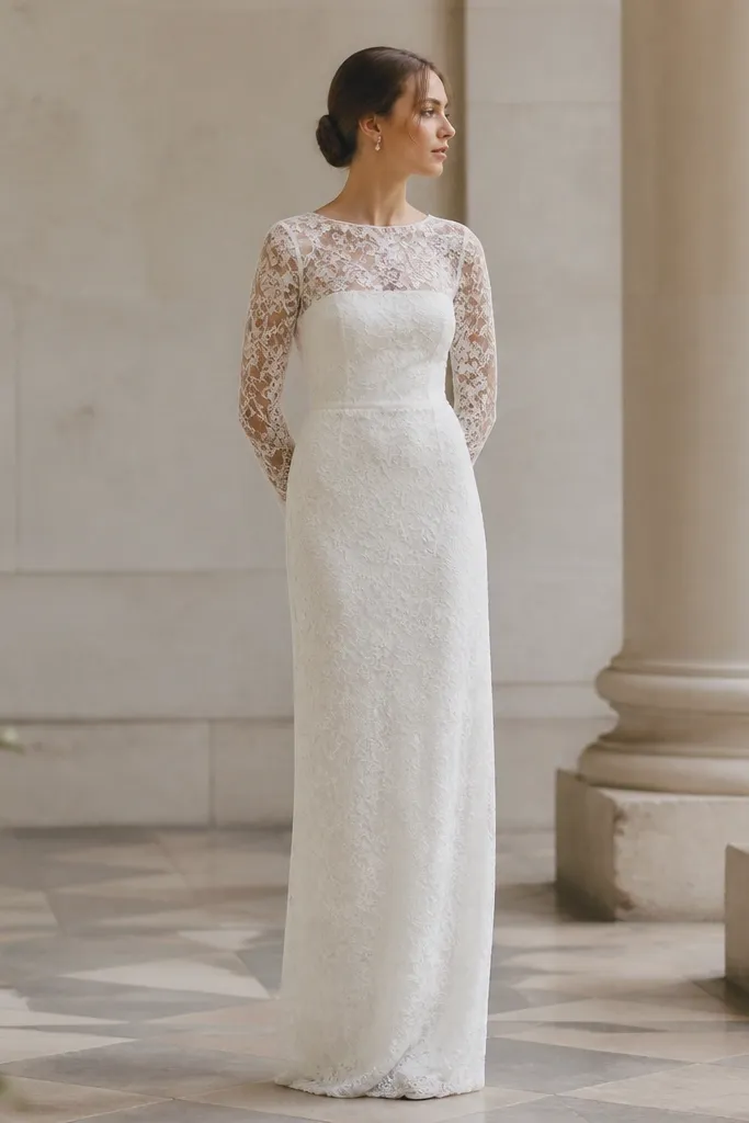 A column-style wedding dress with a high waist seam and long lace sleeves. The lace overlays the top and flows down the column silhouette, with a clean, narrow hemline and minimal train.